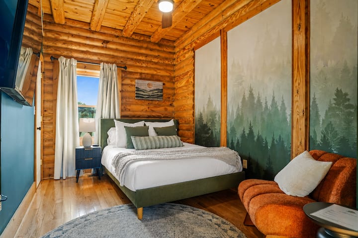 A queen bedroom with a nature-inspired forest accent wall and a reading chair