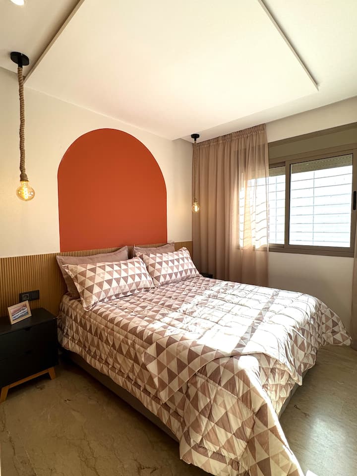 Chambre principale chaleureuse : un havre de paix lumineux avec un lit double confortable, un éclairage moderne et des tons terre chauds. Parfait pour les couples ou les voyageurs en solo à la recherche de repos et de confort au cœur de Rabat.