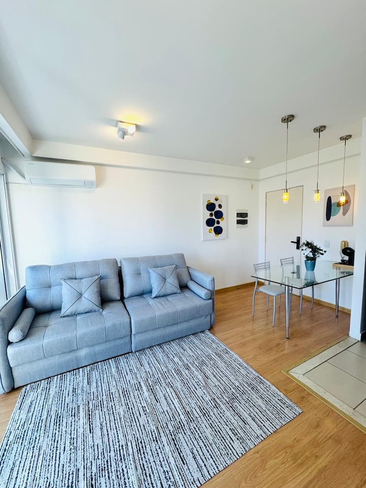 Sala integrada com design clean e iluminação natural abundante, criando um ambiente leve e convidativo. Com ar condicionado e varanda ampla. Conforto e praticidade se unem para momentos relaxantes e bem aproveitados.