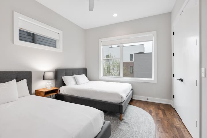 Clean, modern twin-queen bedroom with two plush beds, large window, and soft lighting—perfect for friends or families sharing in comfort.
