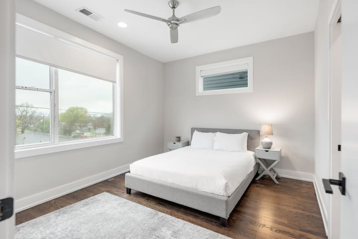 Bright queen bedroom with large window, ceiling fan, soft linens, and modern nightstands—cool, quiet, and perfect for a comfortable night’s sleep.