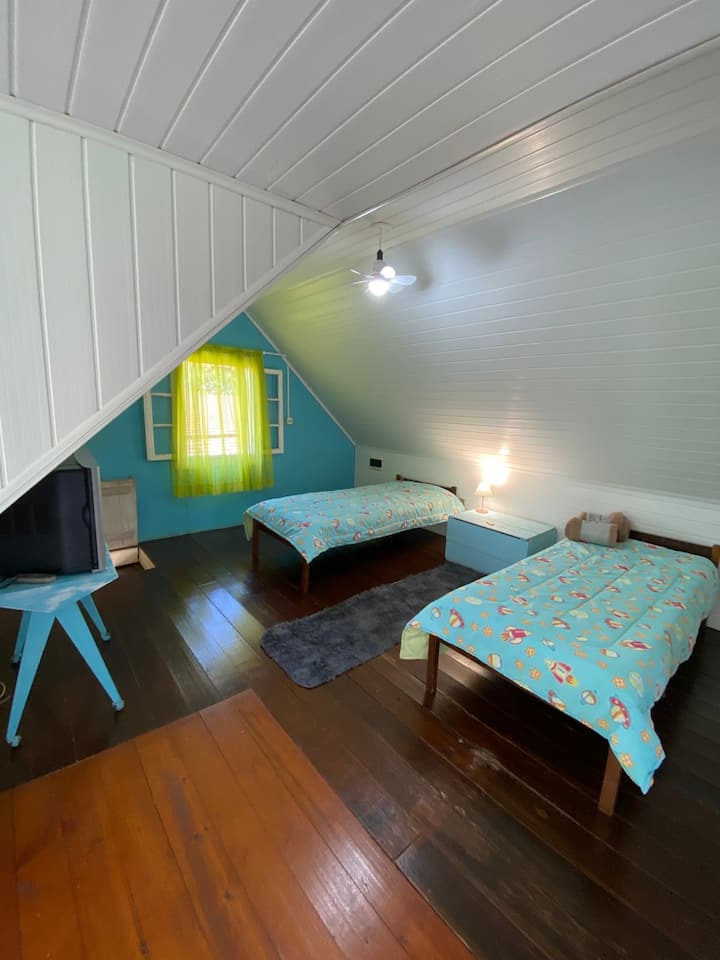 Primeiro quarto no andar superior, com 2 camas de solteiro e acesso direto à sacada. Espaço arejado e iluminado, perfeito para descansar apreciando a vista da natureza.