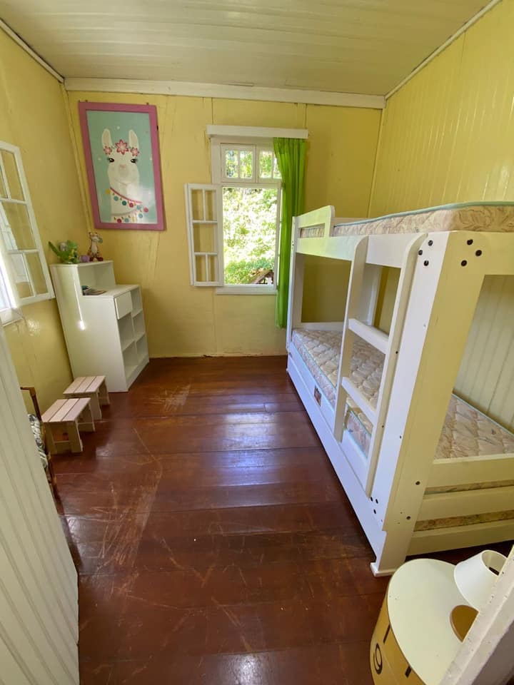 Segundo quarto do 1º piso, decorado com motivos infantis, equipado com triliche (3 camas) e escrivaninha. Espaço leve e alegre, ideal para crianças ou grupos.
