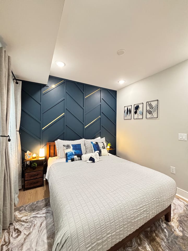 Este dormitorio sereno cuenta con una elegante pared azul decorativa, lujosa ropa de cama y cálida iluminación para un refugio relajante y de primer nivel.