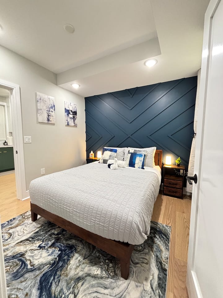“Un dormitorio tranquilo y elegante resaltado por su llamativa pared azul y su decoración suave y moderna”.