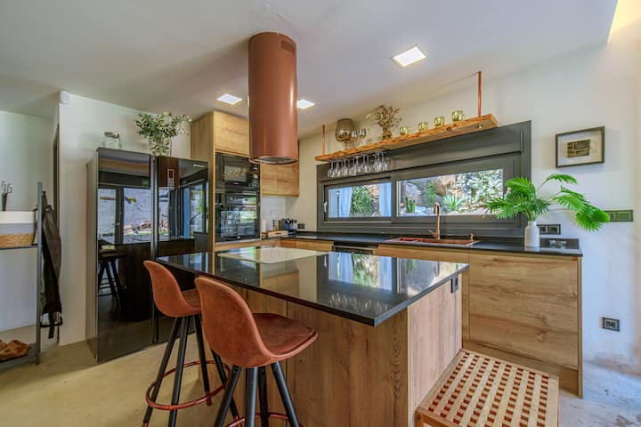 Cocina completa con isla: placa de inducción, horno, microondas, lavavajillas y campana de cobre.