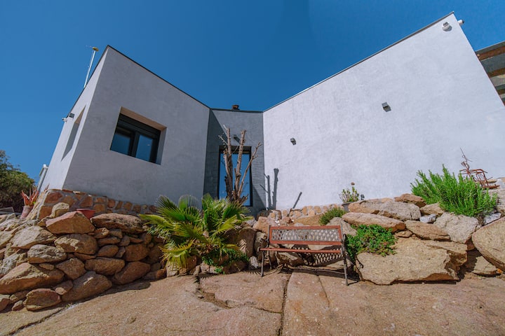 El jardín entre grandes rocas de La Atalaya, con césped y zonas de sombra.