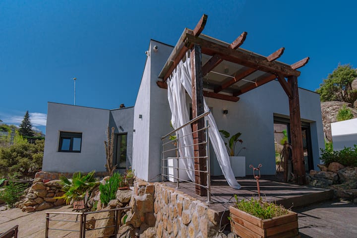 Pérgola de madera en la entrada, con mobiliario de exterior para el aperitivo.
