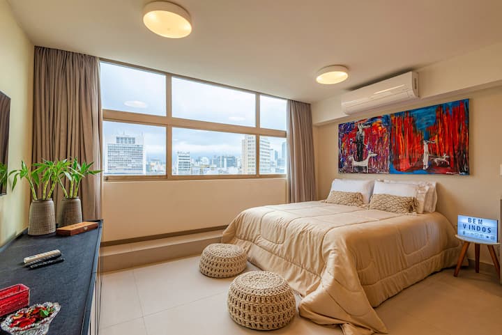 Dormitorio equipado e integrado con cama doble, aire acondicionado, televisor inteligente, cortinas opacas y ropa de cama completa, en un ambiente luminoso y acogedor con una amplia vista de la ciudad.