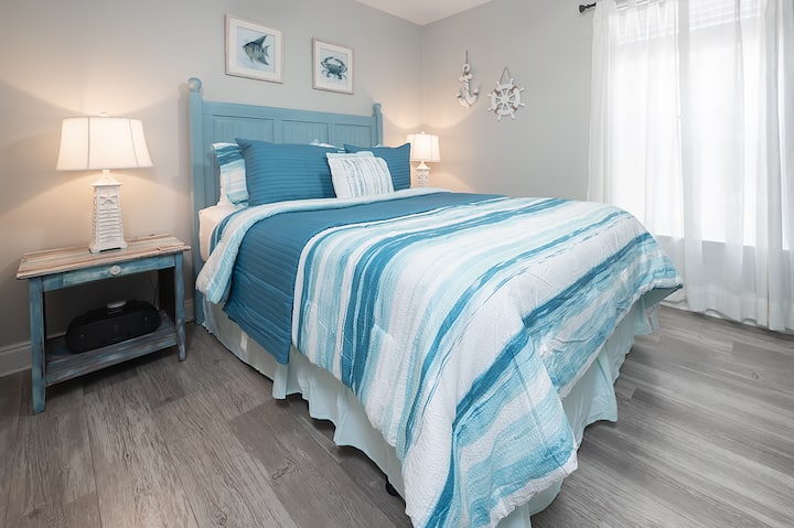 Krásne zariadená spálňa s manželskou posteľou, posteľnou bielizňou inšpirovanou oceánom a príjemným osvetlením – vaše pobrežné útočisko.