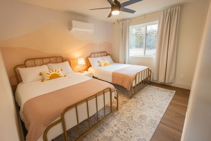 Downstairs bedroom features two full beds, comfortable bedding, extra pillows, blankets, clothes storage (with hangers), warm lighting, nightstand, mini split air conditioner / heater, electric wall heater, and full bathroom next door in hallway.
