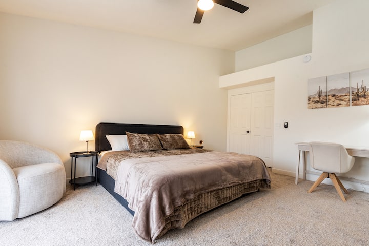 Suíte principal espaçosa com uma cama king size macia, área de estar aconchegante e uma mesa dedicada para trabalho ou tempo de silêncio. Grandes janelas trazem bela luz natural e levam ao banheiro privativo.