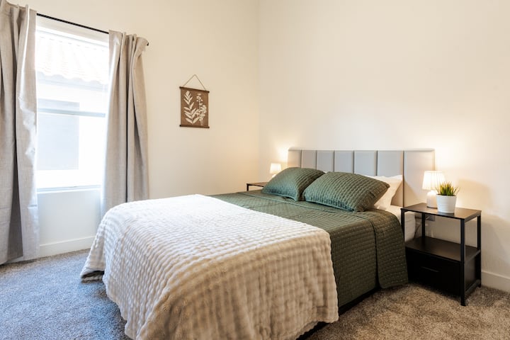 Quarto aconchegante e iluminado com uma cama confortável, roupa de cama macia e cortinas blackout para uma ótima noite de sono. Iluminação acolhedora e decoração minimalista criam um espaço calmo e relaxante para os hóspedes relaxarem.