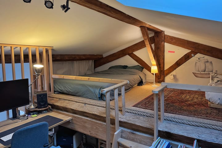 طابق الميزانين الكبير في الطابق العلوي، مع سرير 140 × 200 سم ومنطقة مكتب.