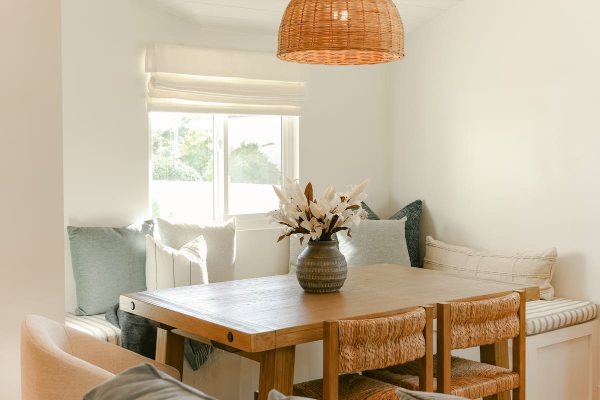 The dining nook with a built in banquette, a wood farm table and a woven pendant at The Sapphire in Pacific Beach, designed by Salt and Sky Lodging Co.