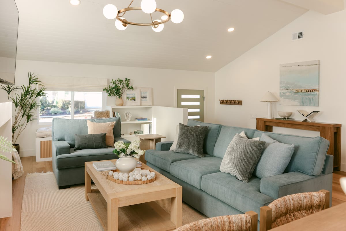 The living room with sage green sofas, a light oak coffee table and a globe chandelier at The Sapphire in Pacific Beach, designed by Salt and Sky Lodging Co.