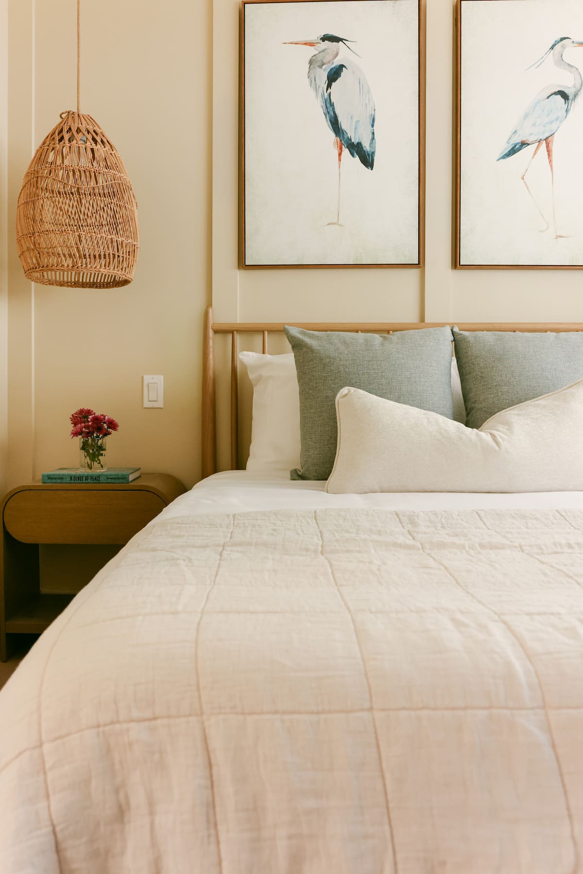 A bedroom with a woven pendant, a wood bed and heron art above the nightstand at The Sapphire in Pacific Beach, designed by Salt and Sky Lodging Co.