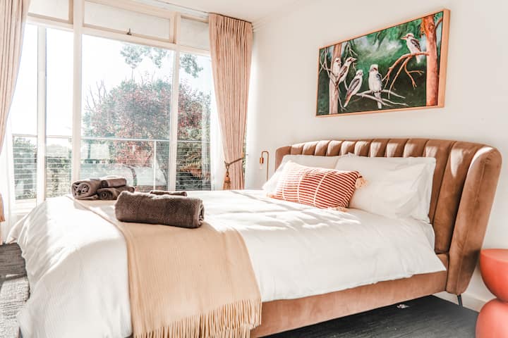 A velvet-bedhead queen room with a statement kookaburra canvas, garden treetop views, and the kind of styling that makes you want to stay an extra night.