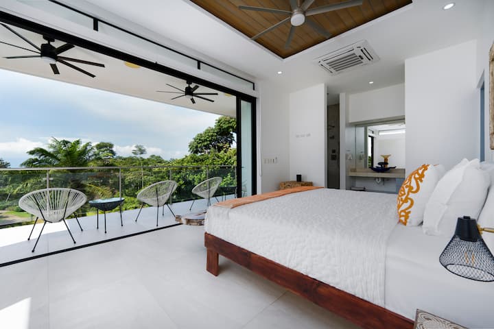 Habitación amplia y luminosa con una acogedora sala de estar con un sofá, tu propio rincón tranquilo para relajarte, leer o recargar energías después de un día de playa o cascadas. Vistas distantes al mar en tu propio balcón privado. Este es el lugar para ver los atardeceres.