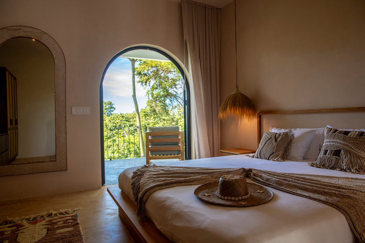 Dormitorio principal n.º 1 con cama tamaño king y acceso a un gran balcón al aire libre con amplias vistas a la selva y al mar. 