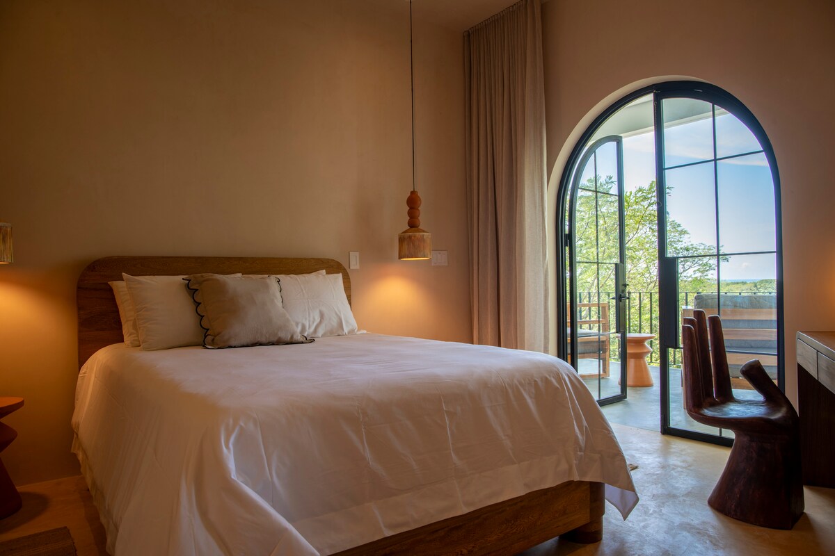 Dormitorio principal n.º 2 con cama tamaño queen. Acceso a un gran balcón con una cama de día y amplias vistas al mar y a la selva. 