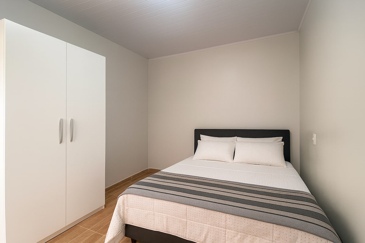 Quarto de apartamento Airbnb em Cascavel com cama de casal, enxoval completo e guarda-roupa, ideal para hospedagem barata.