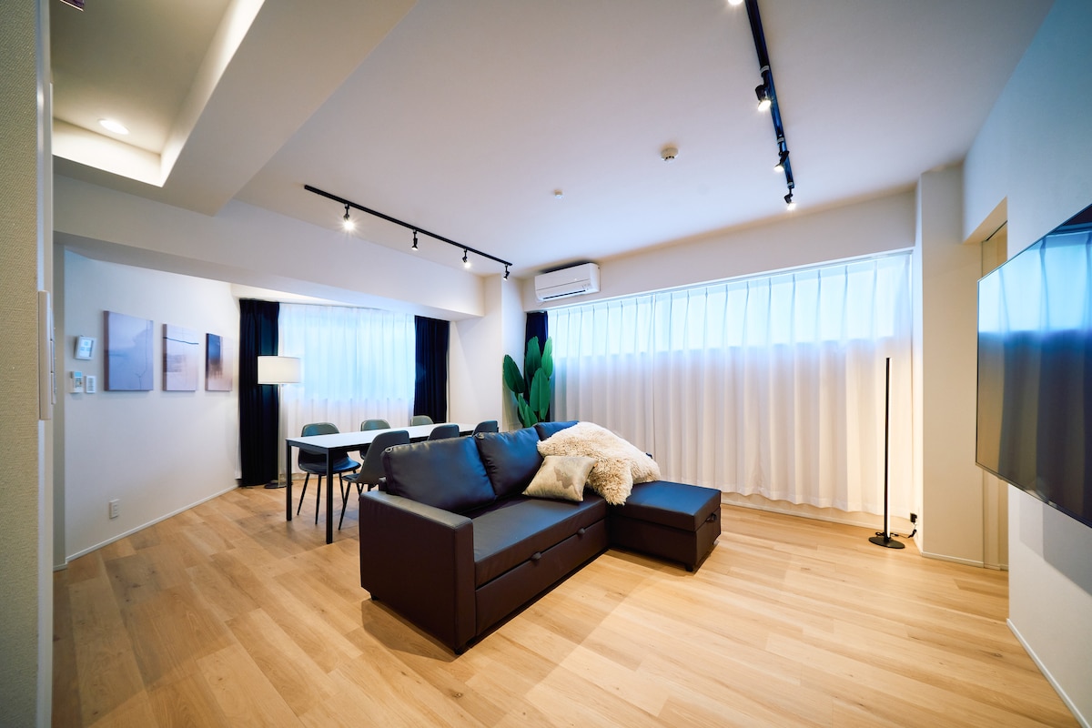 【リビング・ダイニング】約22㎡、ダブルソファベッドとダイニングテーブル6名掛け、65インチ4Kテレビがあり、家族やグループでくつろげる空間です。色を自由に変えられるLEDスタンドライトでシアタールームのようにお使いいただけます。