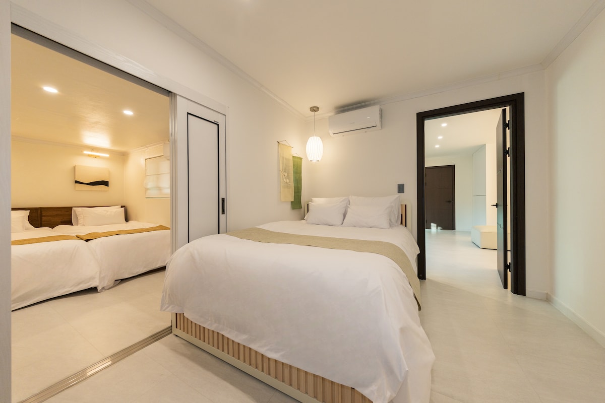 בחדר השמאלי יש מיטת קווין סייז מעץ אגוז ומיטת יחיד, שיוצרים אווירה חמה ויציבה, ומסגרת תמונה עם קו שחור על הקיר מוסיפה תחושה מסוגננת. בחדר השינה הראשי יש מיטה נפתחת עם מיטת קווין סייז ומיטת יחיד, מה שהופך אותו למתאים למבוגרים וילדים. מעל המיטה, תאורת תליון בסגנון קוריאני מסורתי מאירה אור עדין, ויש וילון רקום על משי מסורתי, כך שתוכלו להרגיש את היופי והחמימות הקוריאניים.