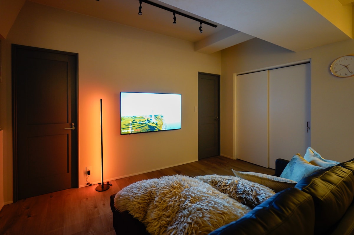 【リビング・ダイニング】約22㎡、ダブルソファベッドとダイニングテーブル6名掛け、55インチ4Kテレビを備えたくつろぎスペースです。色を自由に変えられるLEDスタンドライトでシアタールームのようにお使いいただけます。