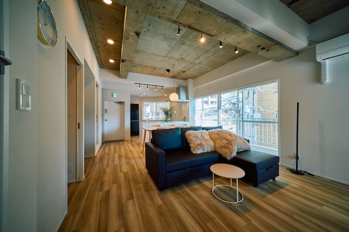 【リビング・ダイニング】約22㎡、ダブルソファベッドとダイニングテーブル6名掛け、55インチ4Kテレビがあり、アイランドキッチンと一体感のあるレイアウトです。色を自由に変えられるLEDスタンドライトでシアタールームのようにお使いいただけます。