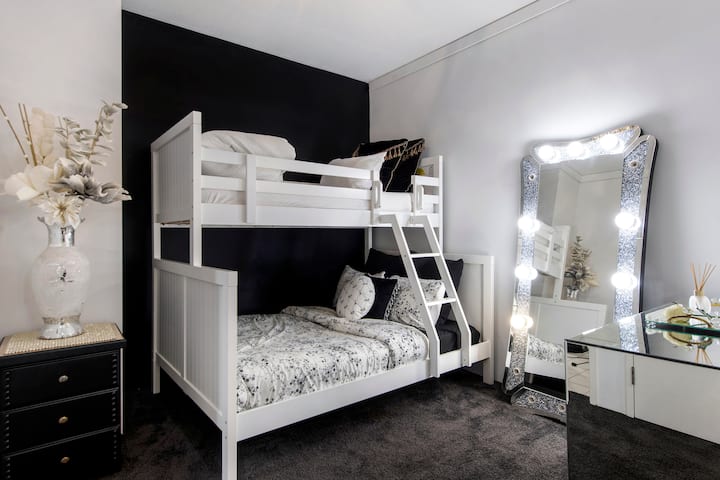 Елегантна втора спална соба со удобен кревет на спрат, гламурозно огледало во холивудски стил и простор за тоалетирање, како и дизајнерски детали насекаде.