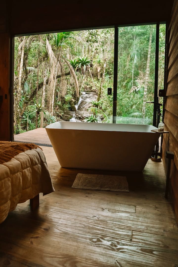 Banheira para 2 pessoas com água quente mineral, de frente para a cachoeira e o riacho de águas cristalinas — um cenário raro, cercado pela Mata Atlântica nativa.