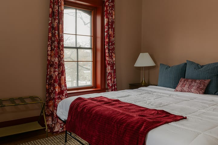 Cama tamaño king vestida con flores de color burdeos y mantas de terciopelo. Vistas a la colina de Loudonville, portaequipajes, mesita de noche: comodidad de grado hotelero en todas las habitaciones.