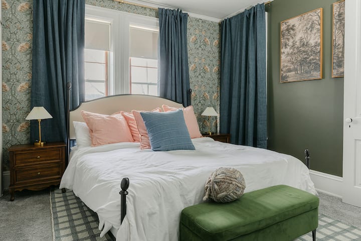 Suite principal con papel tapiz botánico seleccionado a mano y arte vintage. Cama tamaño king, cortinas opacas, ropa de cama de calidad hotelera para reuniones de 10 huéspedes.