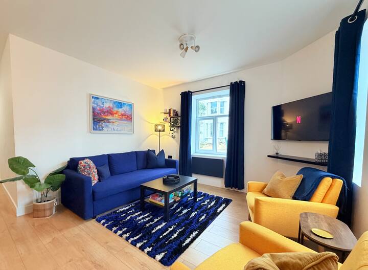 A bright & comfortable living room, with a large sofa-bed, 2 armchairs, games, books, smart TV and tasteful artwork.