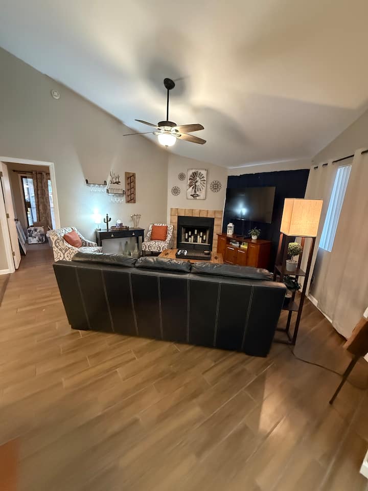 Living room including fireplace, leather couch with fold out bed inside, ceiling fan, decorative seating, television, and lamps