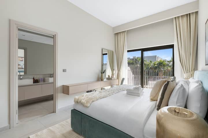 Cama bien hecha con tonos suaves y acceso al balcón