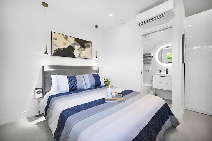 Dormitorio sereno con ropa de cama en capas, iluminación suave y acceso directo al baño.
