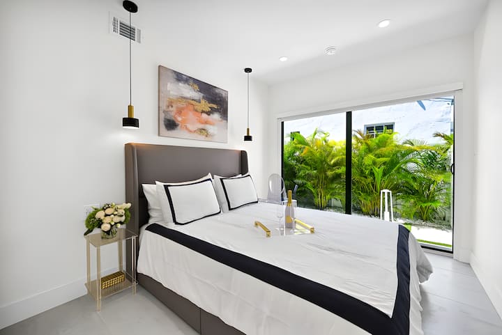 Elegante dormitorio con cama tamaño king, luces colgantes, obras de arte y puertas correderas a la vegetación.