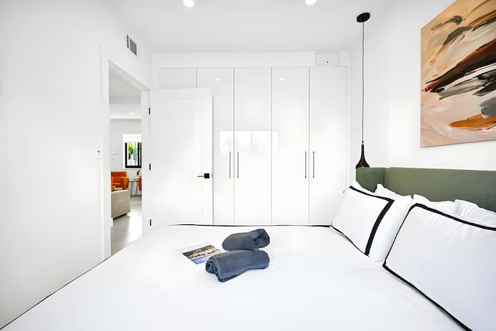 Amplio dormitorio con sábanas frescas, iluminación moderna y armarios de piso a techo.