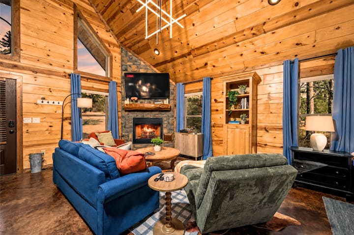 Cozy vaulted cabin living room with stone fireplace and wooded views
