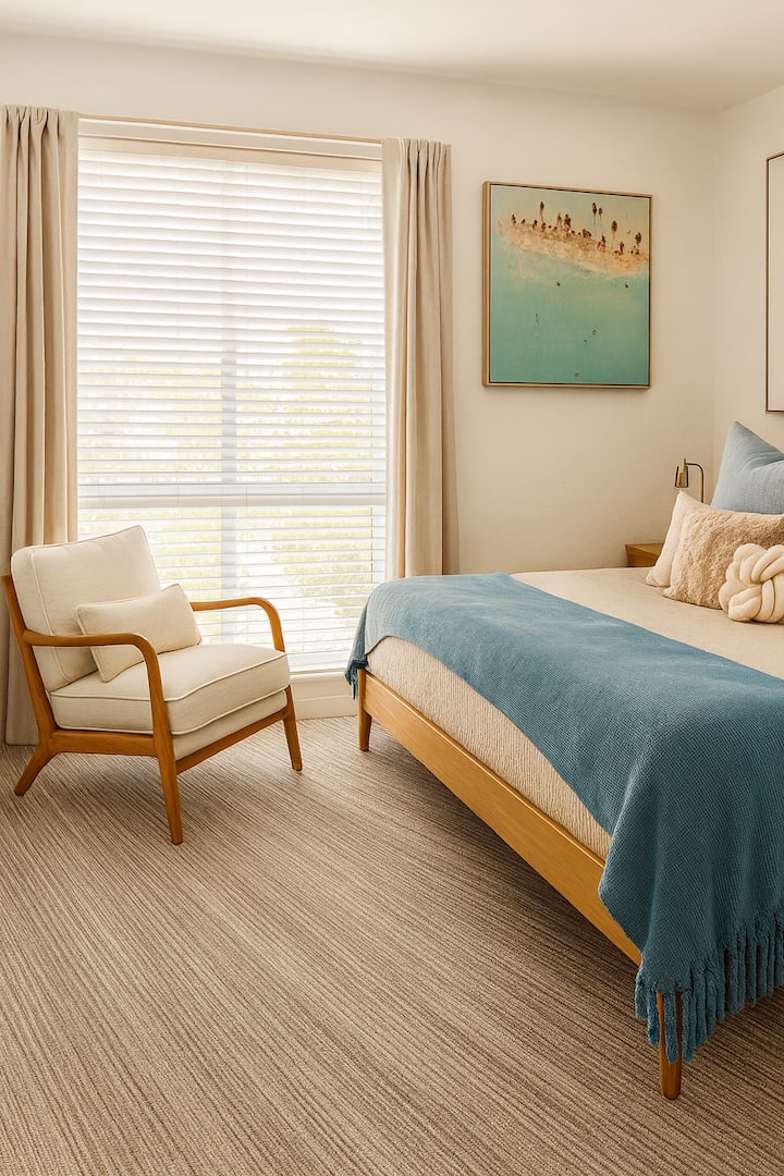 Svetlá spálňa plná prirodzeného svetla s manželskou posteľou s elegantnou posteľnou bielizňou. Kreslo pri okne, jemné modré prvky a vankúše s textúrou vytvárajú pokojný a vzdušný pocit – moderný, príjemný a dokonale navrhnutý na odpočinok a relax.