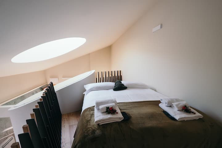 Bračni krevet na međukatnom prostoru s pogledom na glavni apartman: svijetao, udoban i arhitektonski jedinstven otvoreni prostor. Spavanje u ovom smještaju doživljaj je koji objedinjuje vrhunski dizajn i panoramski pogled.