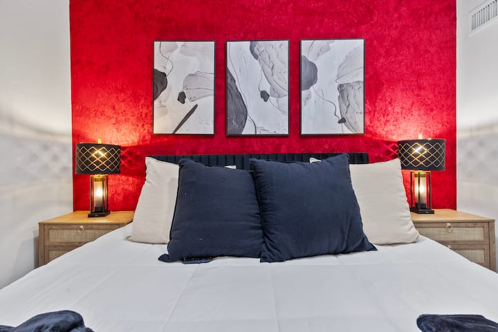 חדר שינה גדול ונועז, עם מרקם עשיר, תאורה חמה ואומנות אוצרתית - מעוצב כך שירגיש דרמטי, אינטימי ומפואר.