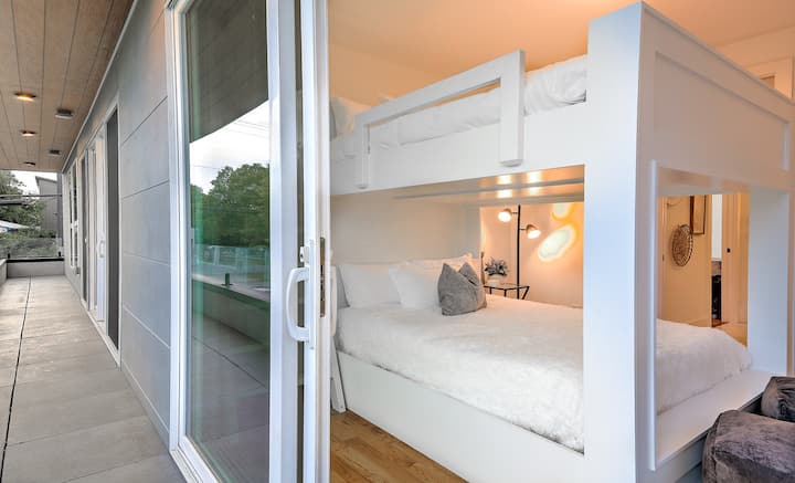 Bright, modern bunk bedroom with custom built-in bunks and plush bedding. Sliding glass doors open to a private balcony, filling the space with natural light—perfect for families or groups seeking comfort, style, and flexible sleeping arrangements.