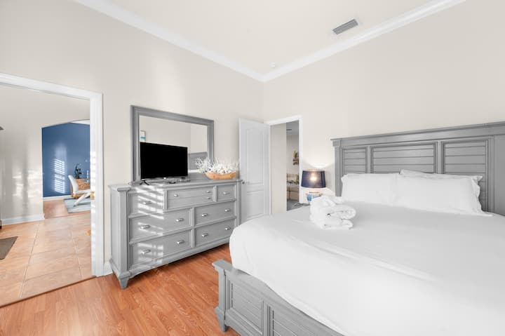 Quarto iluminado e aconchegante com cama king size, cômoda, TV e acesso ao banheiro.