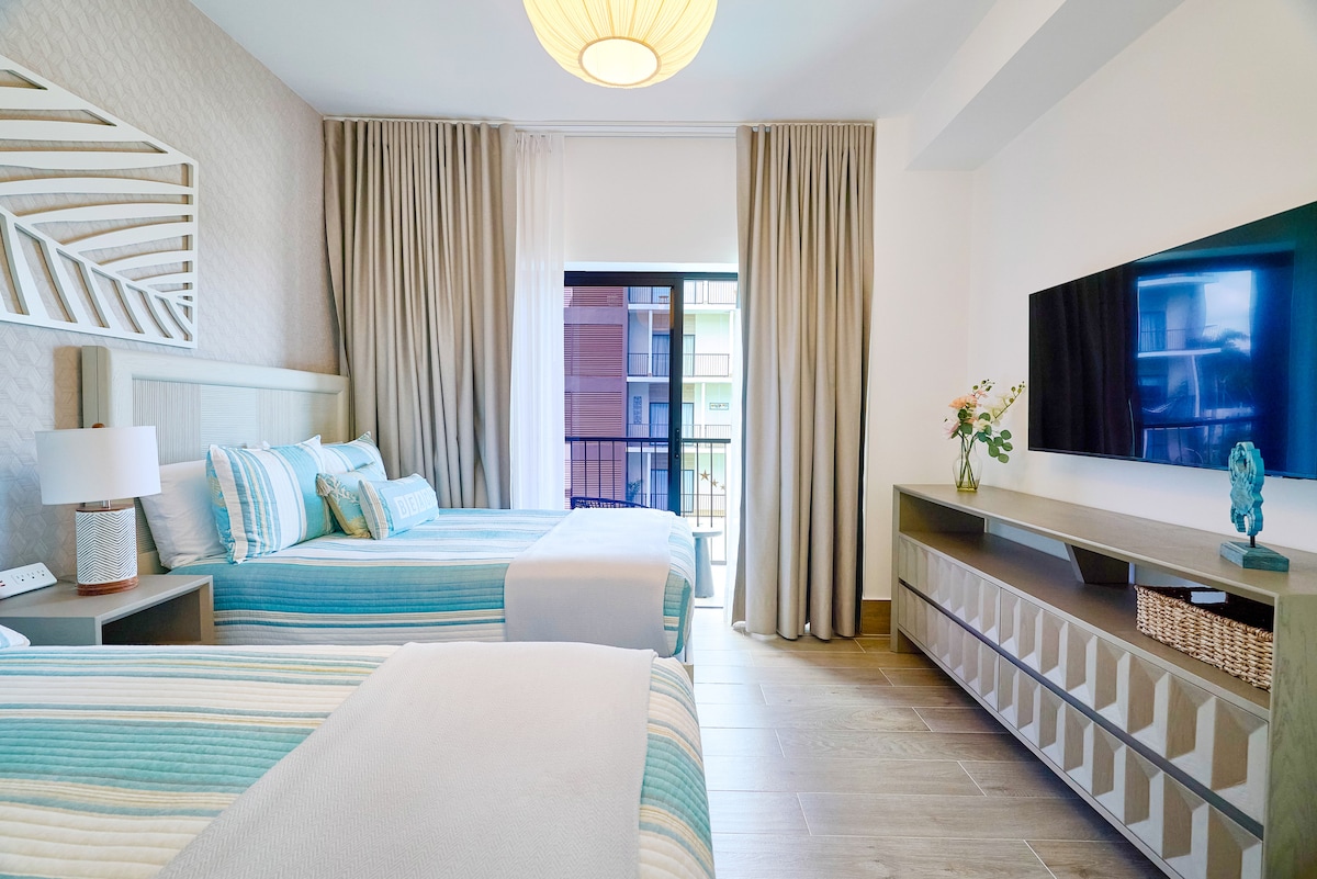 غرفة نوم ثانوية مشرقة مع سريرين مزدوجين مريحين وستائر تعتيم وتلفزيون 50 بوصة وإمكانية وصول خاصة إلى الشرفة. مثالية للعائلات، وتوفر إقامة مريحة مع بياضات ناعمة وإضاءة هادئة وأجواء ساحلية مريحة.