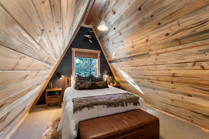 Upstairs loft bedroom featuring a comfortable queen bed, warm wood finishes, and a cozy A-frame feel—perfect for a peaceful night’s sleep.