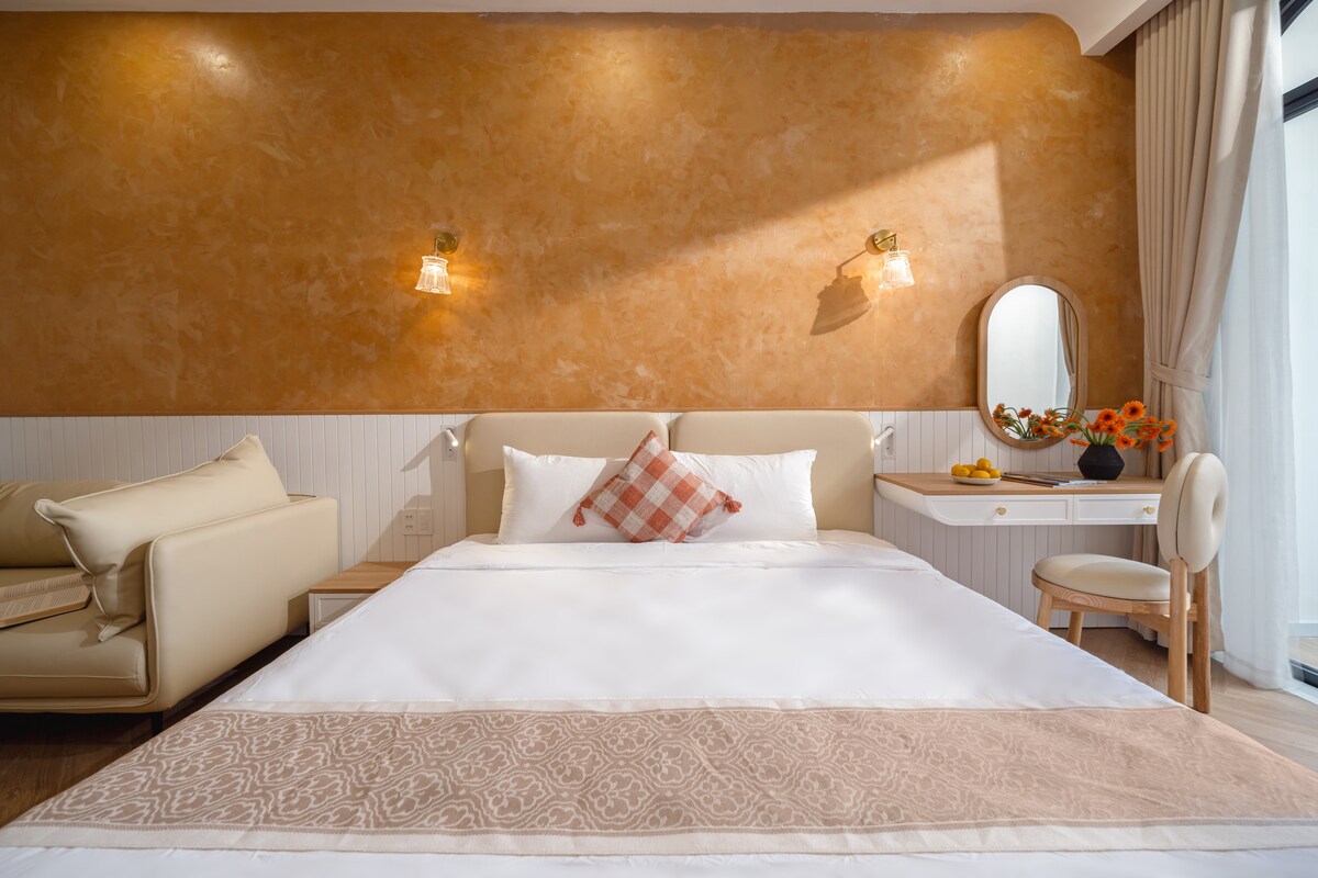 Habitación principal en la parte delantera del 3er piso con una cama King de 1,8 m, balcón a la calle y al patio delantero, baño en suite con bañera grande, sofá suave, grandes ventanales, escritorio, televisor inteligente, aire acondicionado, armario, iluminación cálida y ropa de cama de primera calidad para mayor comodidad.