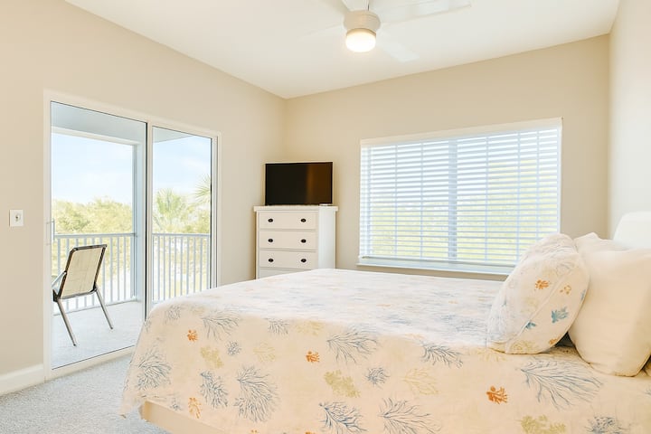 Habitación luminosa para huéspedes con ropa de cama con motivos costeros, una ventana grande y una puerta corrediza de vidrio que da al balcón. Disfrute de vistas espectaculares, un ventilador de techo, un televisor de pantalla plana y un ambiente tranquilo, perfecto para relajarse después de días soleados en Fort Myers Beach.